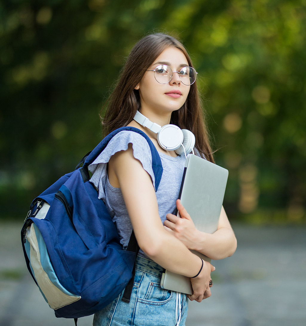 Cheerful attractive woman with backpack and notebooks standing and smiling in park